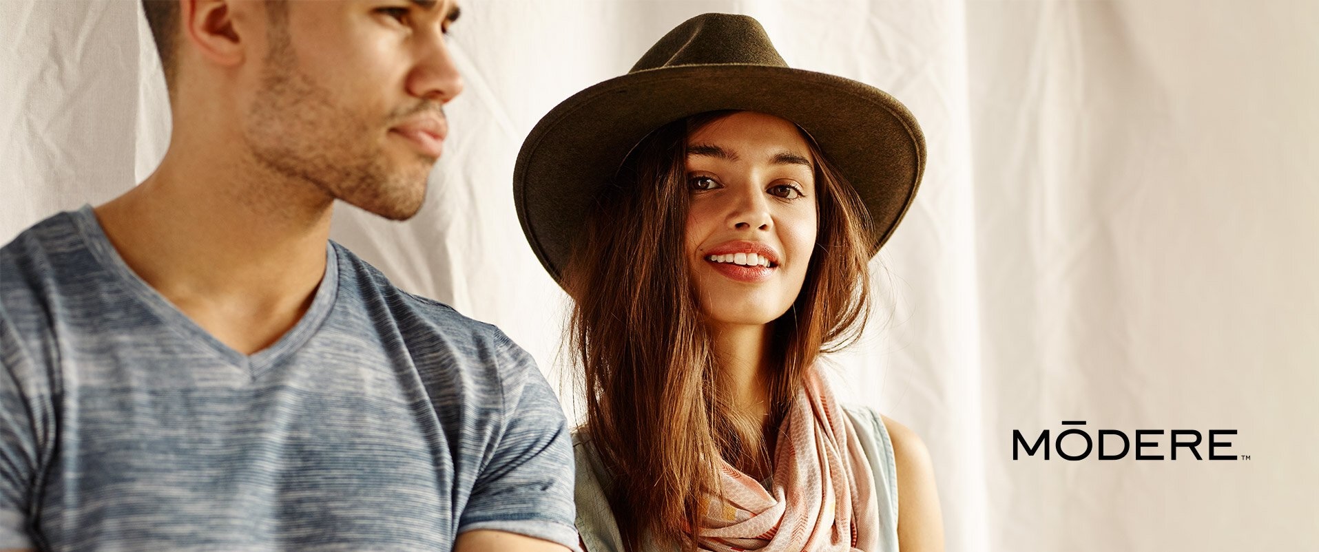 A man and a woman in a wide-brim hat, part of the Modere lifestyle brand campaign, with the Modere wordmark.